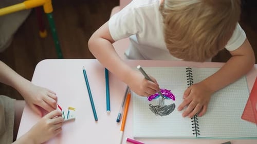 Two Children Drawing Together at a Pink Table