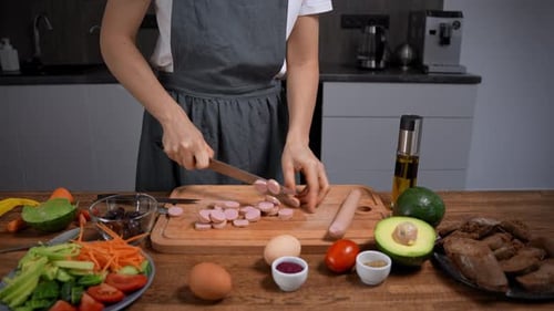 Woman cuts sausage for salad in kitchen