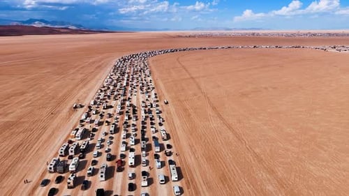 Numerous cars and campervans stand in a curved line along the desert.