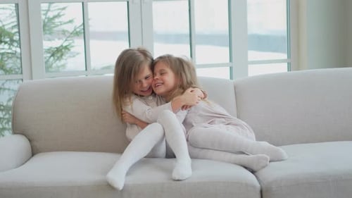 Two Young Girls Embracing on a White Couch