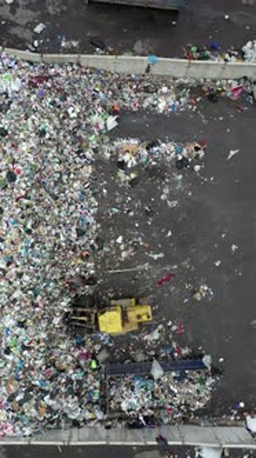 Vertical of Aerial Shot of the Bulldozer Moving the Garbage and Trash in the Landfill Flattens It