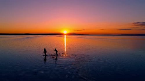 Silhouetted Figures Wading in Ocean at Sunset