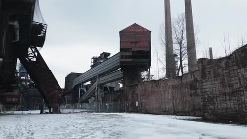 Desolate, snow-covered, abandoned industrial site with rusted structures, a tall brick building, and