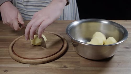Der Koch nimmt geschälte Kartoffeln aus einer Schüssel und schneidet sie in Streifen. Kein Gesicht.