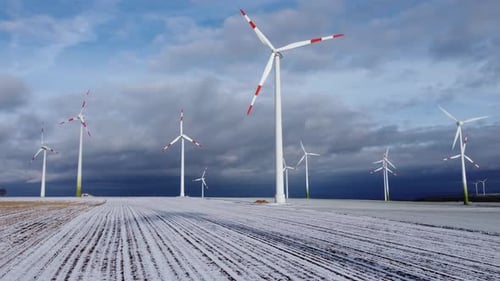 Aerial low angle wide shot of snowy Renewable Energy Wind Farm Wind Turbines lighting in sunlight. W