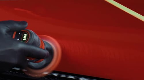Close up of man with black latex gloves polishing red paint on car with a small polishing