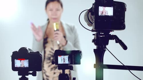 A female television show host does a sound check with a microphone - focus on cameras in the foregro
