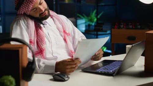 Man Working at Desk Talking on Cellphone at Night