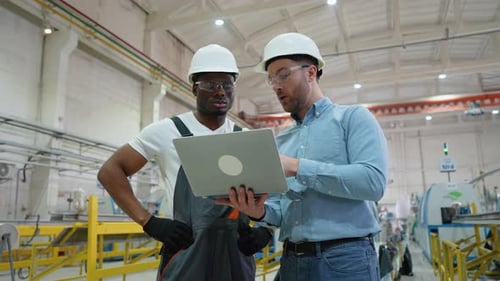 Two Diverse Factory Workers Supervisor and Subordinate Working and Discussing Manufacturing Plan in