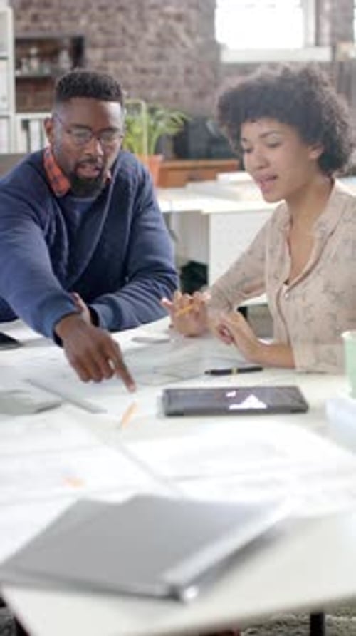 Vertical video of diverse colleagues discussing work with documents in office in slow motion