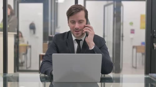 Business Man Talking on Phone While Working on Laptop