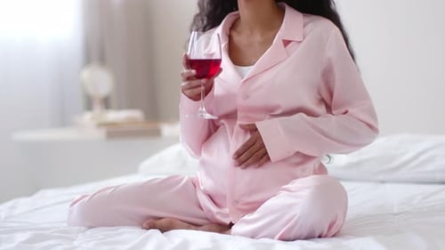 Pregnant Woman Relaxes on Bed with Red Drink