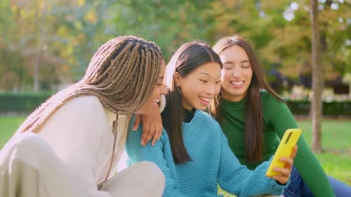 Three Friends Sharing a Mobile Phone in the Park