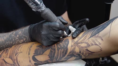 The process of tattooing with a tattoo machine with a woman's face on a man's hand in a tattoo.