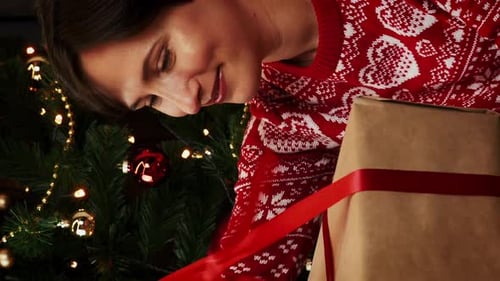 Woman Unwraps Christmas Gift by Tree