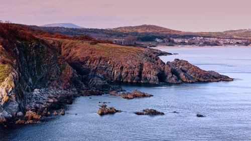 Calm water of the sea at the rocks of the coast. Cityscape on the shore at backdrop. Aerial view.