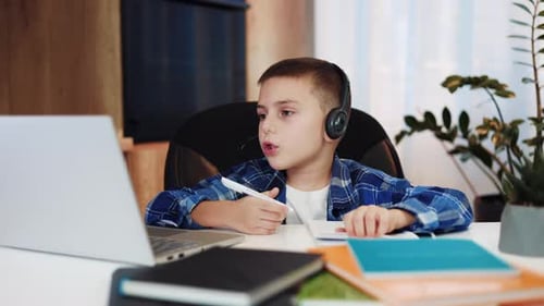 Child Using Laptop and Headset for Elearning at Home with School Equipment