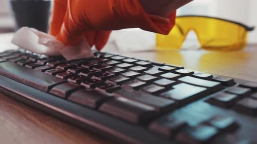 Hands in gloves cleaning and sanitizing computer keyboard