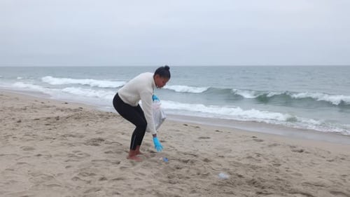 Woman picking up litter from the beach.