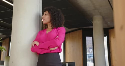 Confident businesswoman in pink blouse standing with arms crossed in office
