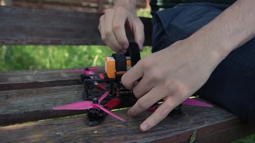 Pilot Strapping Battery Of An FPV Drone On Wooden Bench Outdoor. closeup shot
