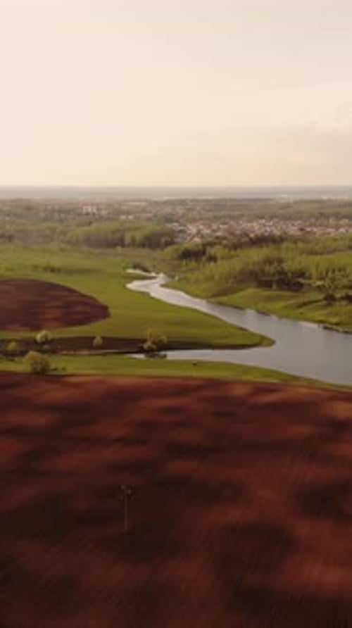 Aerial Panorama of Cultivated Farmland and Winding River Transitioning From Rich Brown Plowed Fields