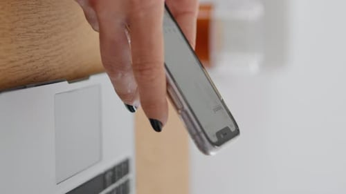 Woman holds mobile phone above a laptop