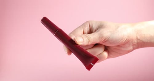 Hand Holds Red Cosmetic Tube on Pink Background