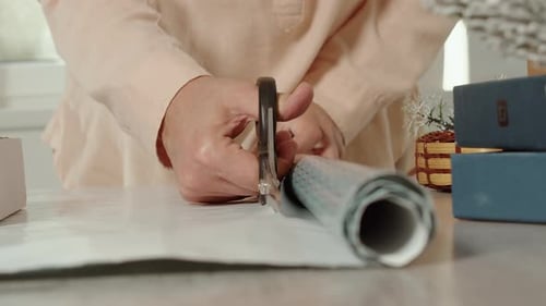 Woman Cuts Wrapping Paper with Scissors on Table