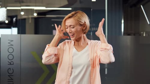Beautiful Blonde Businesswoman or Office Worker Dancing in Office Having Fun