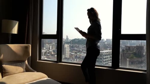 Woman Using Tablet by Window Overlooking City