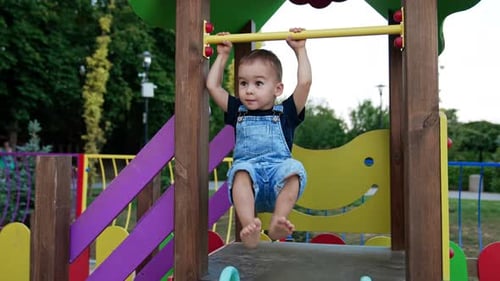 Adorable barefoot baby boy hanging on the horizontal bar.