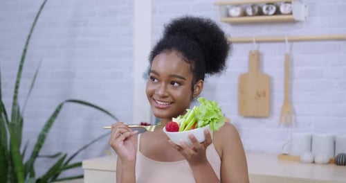 Smiling Woman Eating Salad in Bright Kitchen