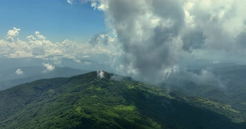 Flying trough white fluffy clouds above green mountain peaks. Beautiful summer sunny day on the high