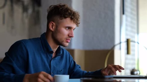 Young Businessman Sitting in Restaurant Texting on Laptop Working Online and Drinking Coffee