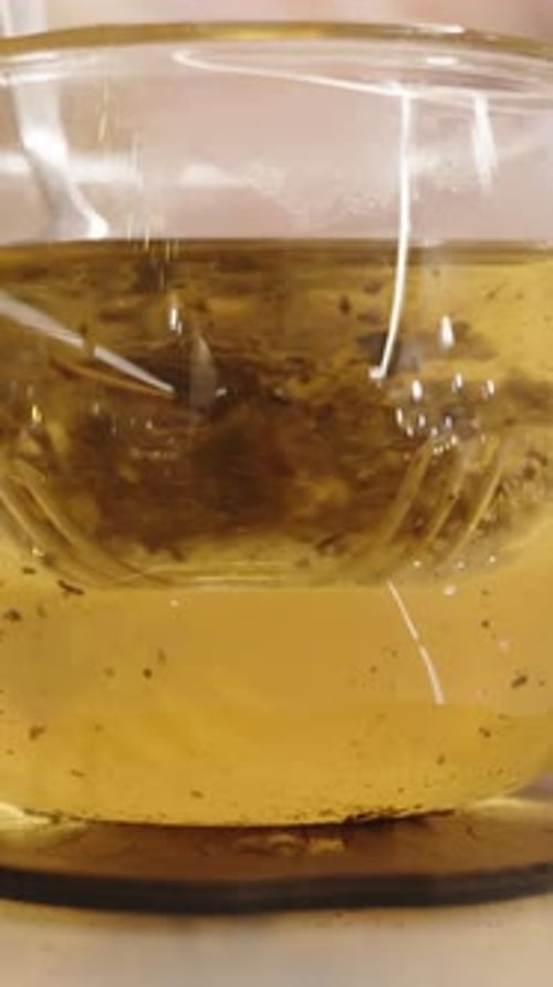 Vertical video. Stirring tea leaves in a cup, and particles falling down. Close-up, slow-motion.