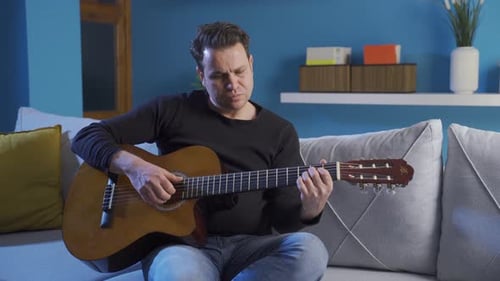 Man Playing Acoustic Guitar on Sofa Indoors