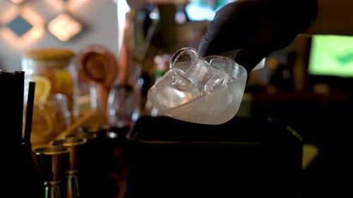 Pouring ice in a glass at a bar. Preparation of a cocktail.