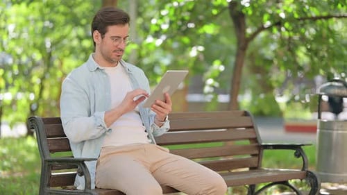 Casual Young Man Using Digital Tablet while Sitting in Park