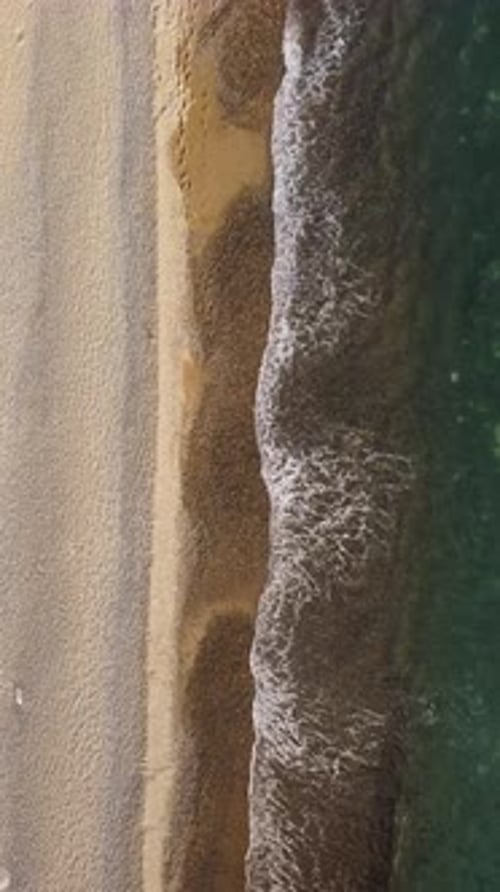 Aerial Vertical View of Beach with Wave Caressing Shore Sun Glare Small Waves on the Water Surface