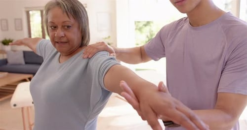 Physiotherapist assisting senior woman with arm stretching exercise in clinic