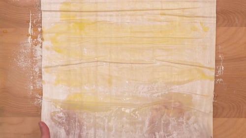 Hands Folding Buttered Dough on Wooden Table