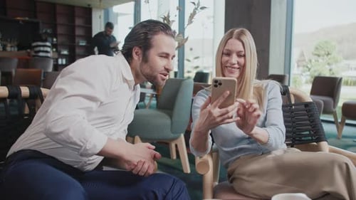 Portrait of the Young Happy Couple with a Smartphone in a Cafe Talking Smiling Sitting Have
