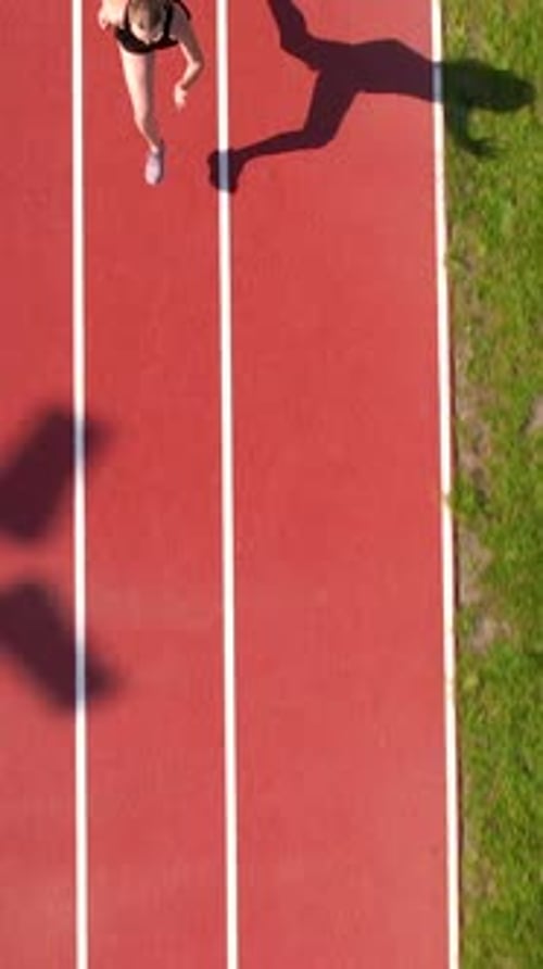 Top Down Aerial View Of Young Woman Running On Red Stadium Track