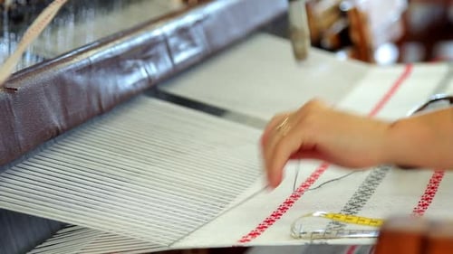 Textilarbeiterin fertigt Musterstoffe auf moderner Webmaschine von Hand