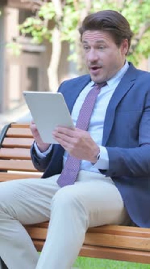 Excited Man Using Tablet While Sitting on Bench
