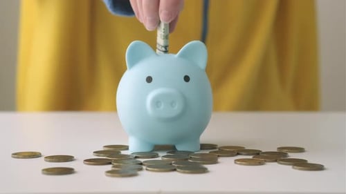 Person in Yellow Jacket Putting Money Into Piggy Bank