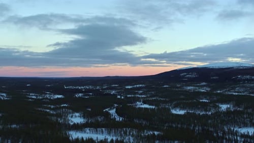 Smooth drone flight over the snowy landscape of sweden with a light red glow at the horizon of the u