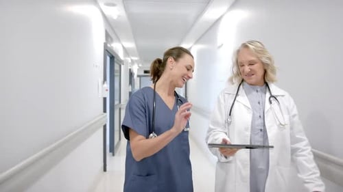 Caucasian female doctors in discussion using tablet in hospital corridor, slow motion