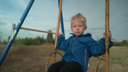 A blond boy sits on a children's swing in the park